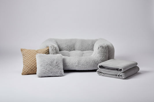 Gray pet bed with a smaller version of itself, a pillow, and a blanket on a white background.